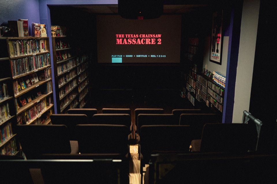 The theater at Austin Video Store from the back row, the seats facing a lit screen and shelves of tapes along both walls